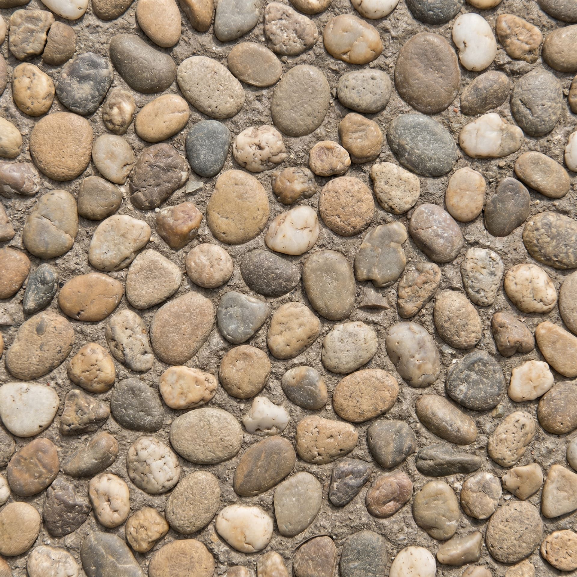 Close-up detail of an exposed-aggregate concrete surface with smooth river pebbles in tan, gray, brown, and white tones embedded in cement paste